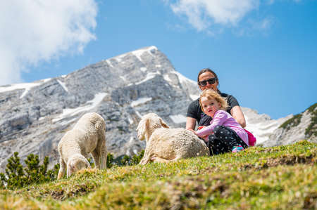 Mother and daughter petting cute sheep in mountain meadow.の写真素材