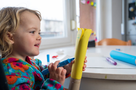 Cute blonde girl paitining with many colors using paintbrush and fingers.