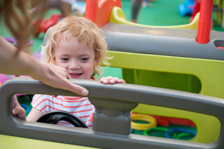 Cute blonde girl riding a plastic car at outdoor playground.の写真素材