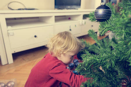 Cute blonde girl decorating Christmas tree with many ornaments.の写真素材