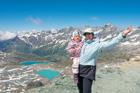 Happy mother holding her daughter surrounded with picturesque mountain landscape.