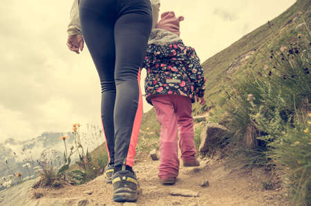 Mother and daughter hiking hand in hand a trail through mountain pastures.の写真素材