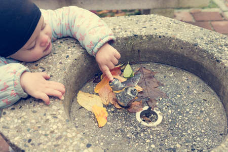 Young girl wearing a black cap exploring drinking station outdoor.の写真素材