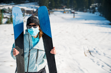Female skier posing with a pait of skis wearing protective face mask.