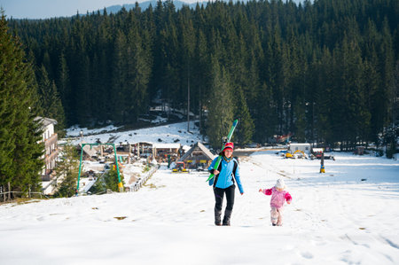 Mother and daughter walking up a ski slope.