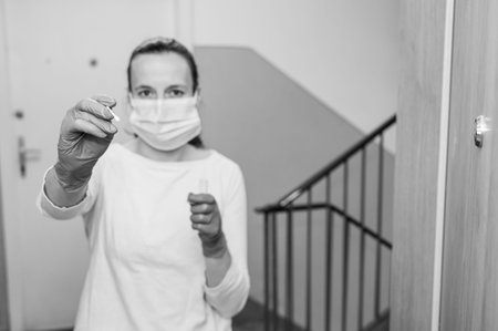 Medical nurse at aparment door with a swab for covid 19 general population testing at home address.
