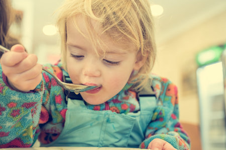 Cute blonde girl eating beef noodle soup in a restaurant with her mother.