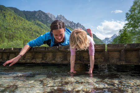 Mother and daughter laying on wooden bridge looking into water.の写真素材
