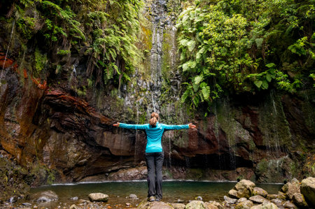 Traveler woman wearing sport jacket and raising hands at waterfall. Travel lifestyle. View from...