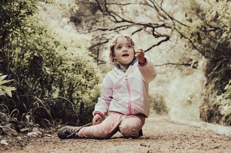 Cute blonde girl sitting on forest trail enjoying the nature and posing.の写真素材