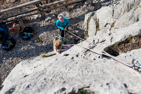 Cute blonde girl rock climbing using top rope with her mother protecting her.