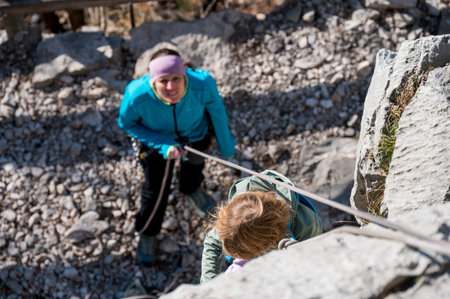 Cute blonde girl rock climbing using top rope with her mother protecting her.