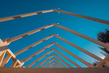Modern wooden roof frame or frames, framework with trusses on a renovated house. Blue sky in the backgroundの写真素材