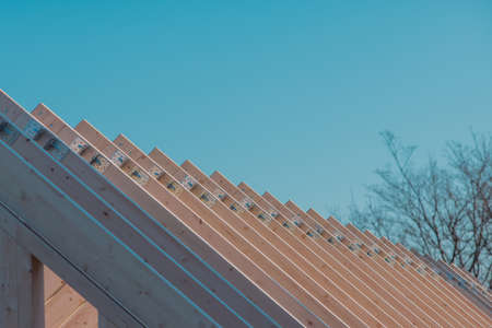 Modern wooden roof frame or frames, framework with trusses on a renovated house. Blue sky in the backgroundの写真素材