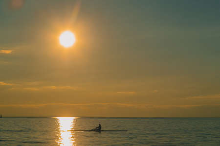 Kayaker or a person in a paddle boat on a lake during evening hours. Romantic leisure activity on the water. Sun about to set into the water.の写真素材