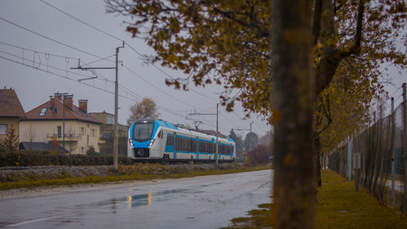 Modern white and blue passenger commuter train passing by in rain. Rainy commute with a modern train in cold and grey weather.の写真素材