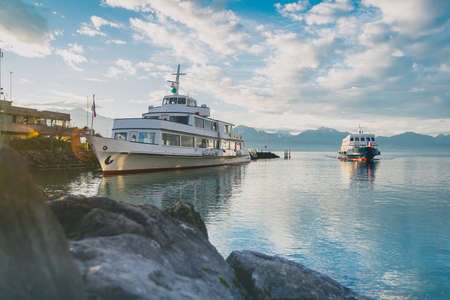Two public ferries or boats on service on Lac Leman in the Ouchy harbor in Lausanne on an early winter morning with some sunshine and clouds.の写真素材