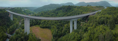 Long and curved span of a highway or motorway viaduct constructed above the valley in cold gray weather.の写真素材