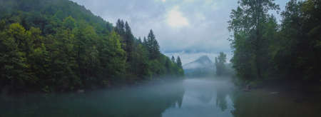 Scary spooky river of Kolpa on a gray dull summer day with clouds and overcast sky with thick fog above the water surface. Scary river sceneの写真素材