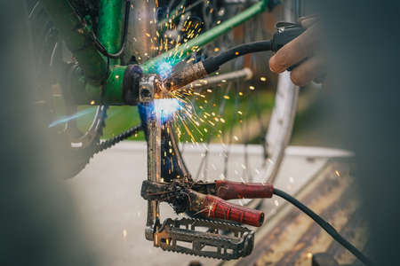Welding an old crank or axle which was broken on an older vintage city bicycle. Man seen using a welding gun on a bicycle crank.の写真素材