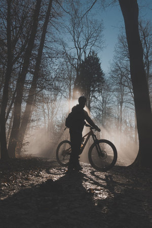 Single mountain biker posing in epical moment with sun rays shining through fog, going uphill...
