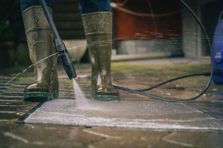 Person cleaning a rug or floor mat with the use of a high pressure water cleaner. Cleaning mats with high pressure jet while wearing plastic bootsの写真素材