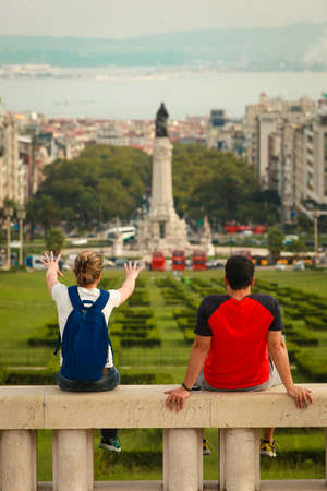 Happy tourist couple with open arms at Miradouro Park Eduardo VII in Lisbon, Portugal, Europe, looking towards gardens in the park with Marquess of Pombal Statue and Avenida de Liberdade in a background on a overcast day.の写真素材