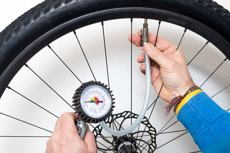 A person is inflating a bicycle wheel with the help of compressed air and a pressure gauge. Wheel and hand seen in the background in soft focus.の写真素材