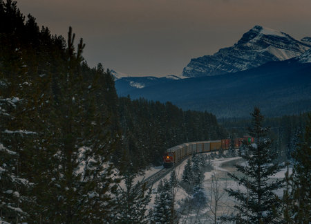 Freight train with containers after picturesque Morant's curve on a cold winter evening with sun just setting behind majestic mountains.の写真素材