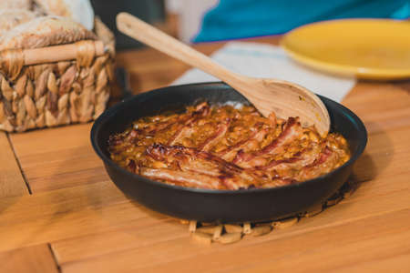 A black bowl of traditional food made of beans prebranac with slices of bacon served at a picnic.の写真素材