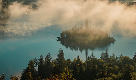 Panoramic photo of lake Bled island with church on a cold hazy foggy early autumn morning from...