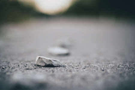 A sharp stone on a asphalt surface of a road. Detail photo of a sharp stone, concept of dangerous hazard for cyclist, roller skaters, skaters and even car tires, waiting to get a punctureの写真素材