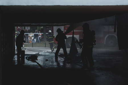 Silhouette of firemen trying to extinguish a garage fire in Ljubljana, Slovenia. A few men under the roof of the garage.の写真素材