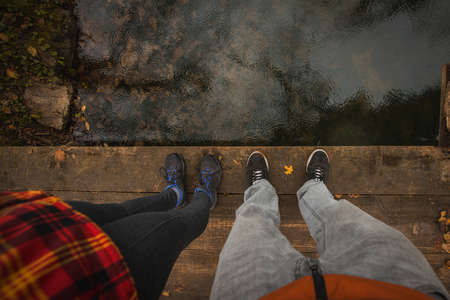Two feet with sport shoes standing on a wooden bridge over calm water with rain drops. Camera looking down towards feet and floor.の写真素材