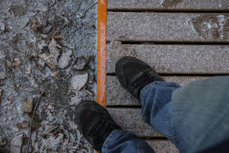 Looking down towards feet in black shoes and jeans standing on light layer of snow.の写真素材