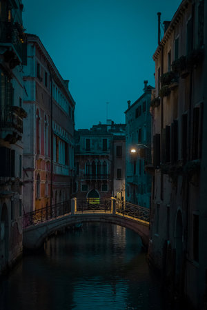 Beautiful small bridge with yellow lighting over a canal in magnificent city of Venice during night time or early evening. Blue hour in Venice, Italy.の写真素材