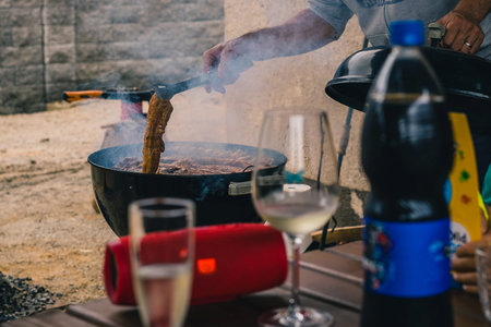 Man opening a smoker barbecue or a charcoal grill oven, to turn kebabs or spare ribs grilling on...