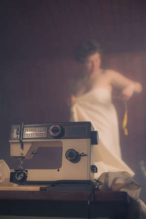 Old retro sewing machine with a woman posing as a model measuring her newly sewn dress which is wrapped around her. Vintage sewing machine and retro crafty woman.の写真素材