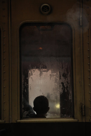 Silhouette of a child's head in a vintage train window with rain droplets on it.の写真素材