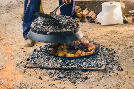 Man opening a sac or podpeka pot covered with charcoal to reveal potatoes and squid or octopus baking inside. Tasty balkan or dalmatian snackの写真素材