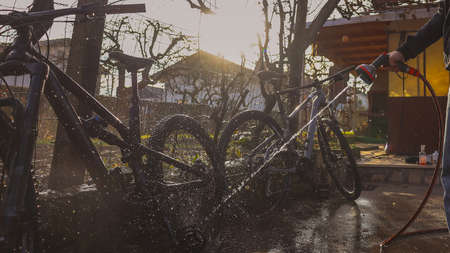 Person cleaning mountain bikes with the aid of a water jet. Panoramic dreamy photo of bicycle cleaning, strong sunlit backlight.の写真素材