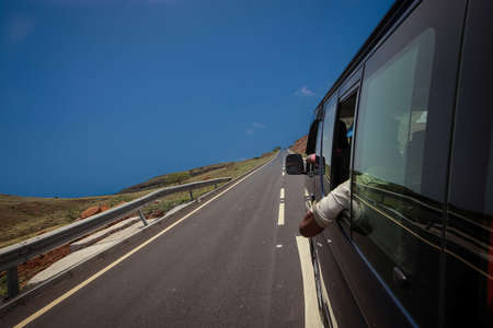 Riding with a blue van in first person on a street on island of Fogo on Cabo Verde islands. Blue sky and sea is seen  in the background.の写真素材