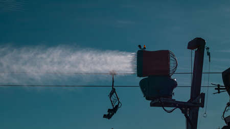 Silhouette of a snow cannon or artificial snow maker on a ski slope on a sunny day. Visible sun flare behind the exhaust of a cannonの写真素材