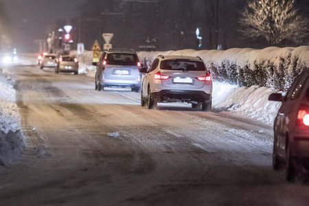 A row of passenger cars in a row on a daily commute on a snowy road during early morning. Early morning commute in snowy conditions with SUV and other passenger cars.の写真素材
