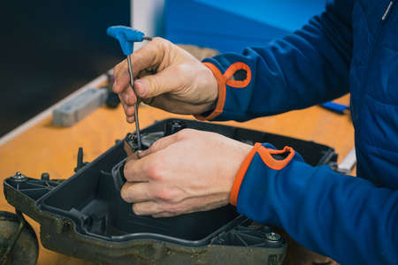 Serviceman stripping robotic lawnmower with imbus tool, motorized lawnmower being serviced on a table after a year of use in the mud and grass. Regular maintenance of robotic lawnmowerの写真素材