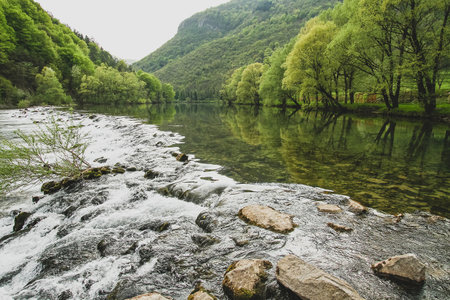 A small stone dam trees and and some hills on Kolpa river, Slovenia.の写真素材