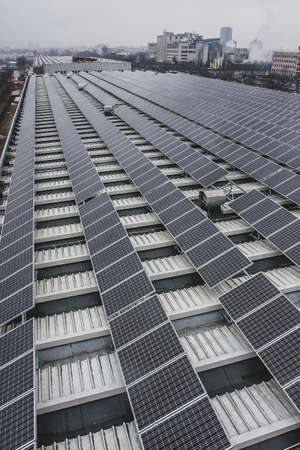 Solar panels installed on a roof of a large industrial building or a warehouse. Industrial buildings in the background. Vertical photoの写真素材
