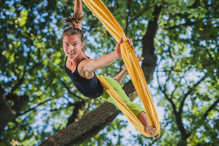 Aerial silk artist performing movements on ropes hanging from trees on a sunny day in Tivoli park, Ljubljana.の写真素材