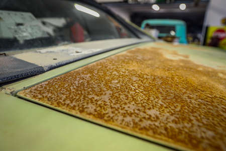Heavily rusted surface of a vintage american lime green muscle car in a car workshop under neon lights.の写真素材