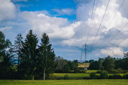 Electrical power lines leading through a field and trees on a cloudy background. Transporting electricity over long distances.の写真素材